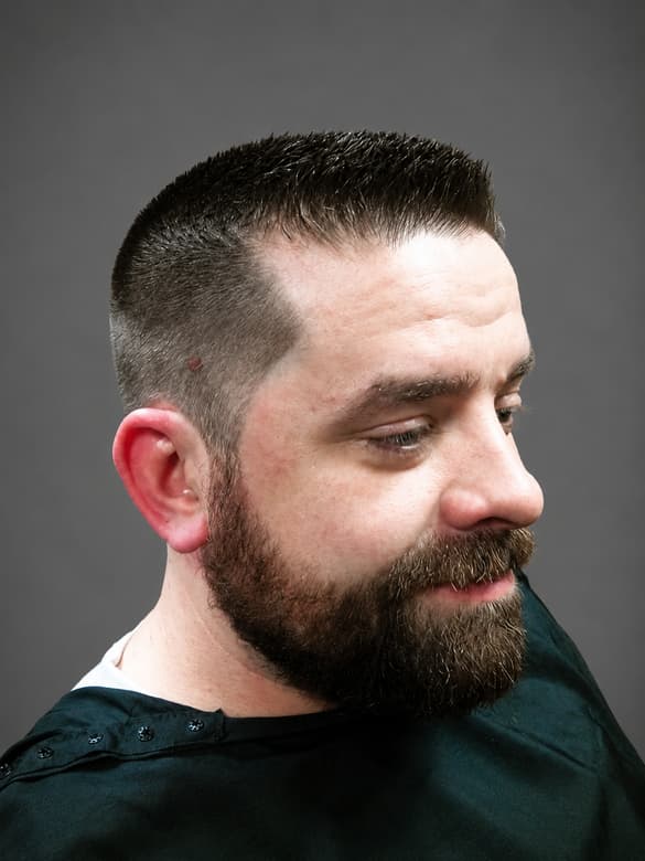 A short crop faded above the ear, with the beard trimmed to a clean line along the cheek.