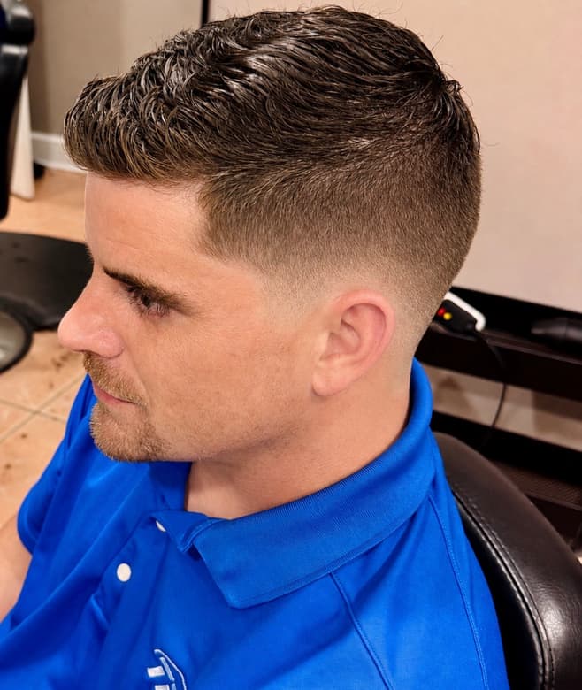 A light brown textured crop faded into short sides, photographed in the studio chair with the clippers on the counter behind.