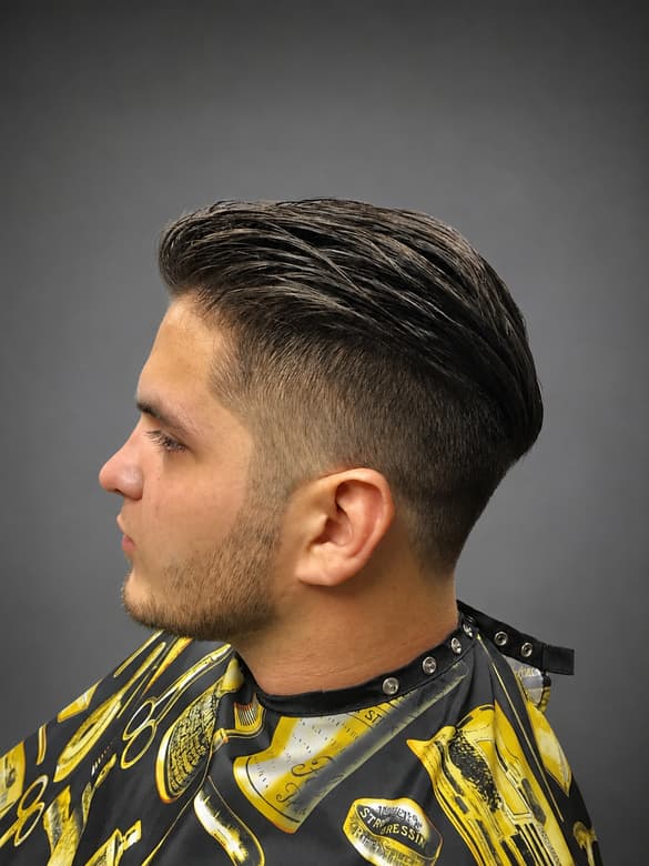 A dark slicked-back cut tapered short above the ear, seen from the side, over a patterned barber cape.