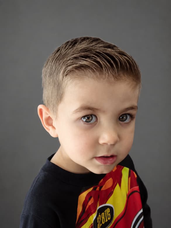 A child’s short cut brushed to one side and tapered above the ear.